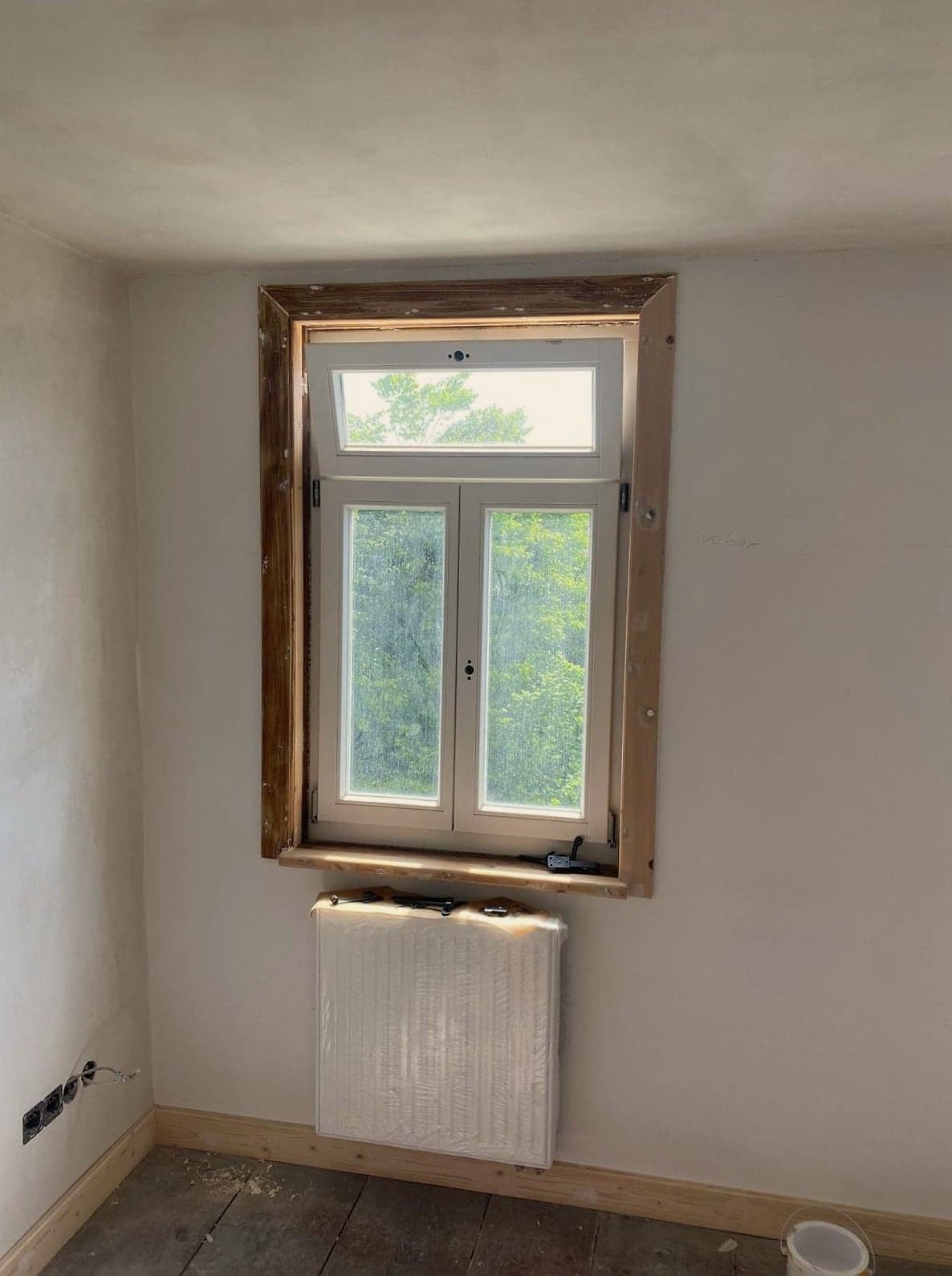 Frisch verputzter Raum mit Holz-Kastenfenster und Heizkörper unter der Fensterbank